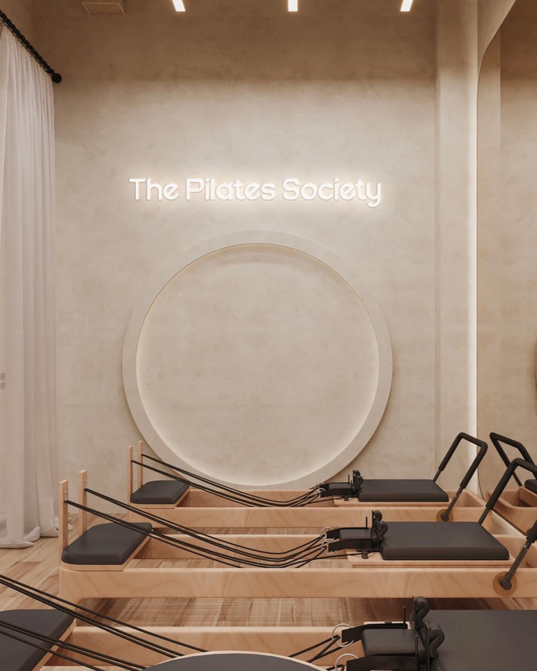 Reformer beds beneath a lit wall feature at The Pilates Society studio in Gombe, Kinshasa.