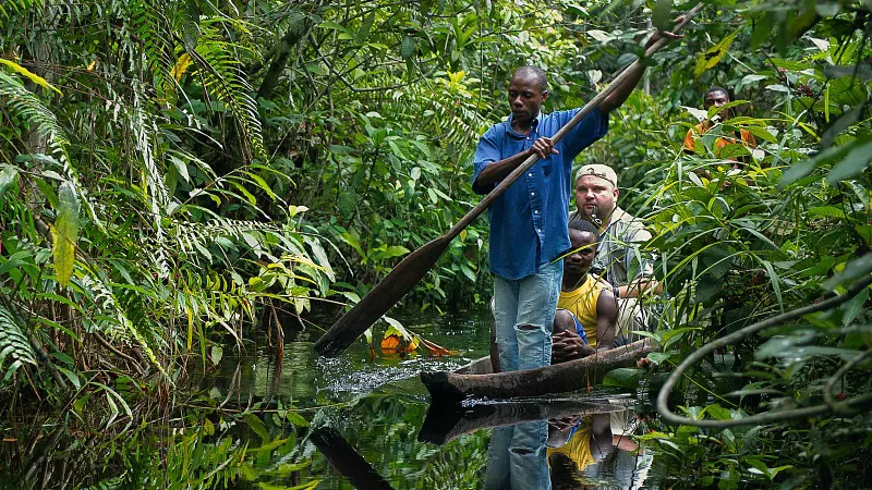 Local guide and travelers paddling a traditional pirogue through dense Congo rainforest waterways — Congo River expedition