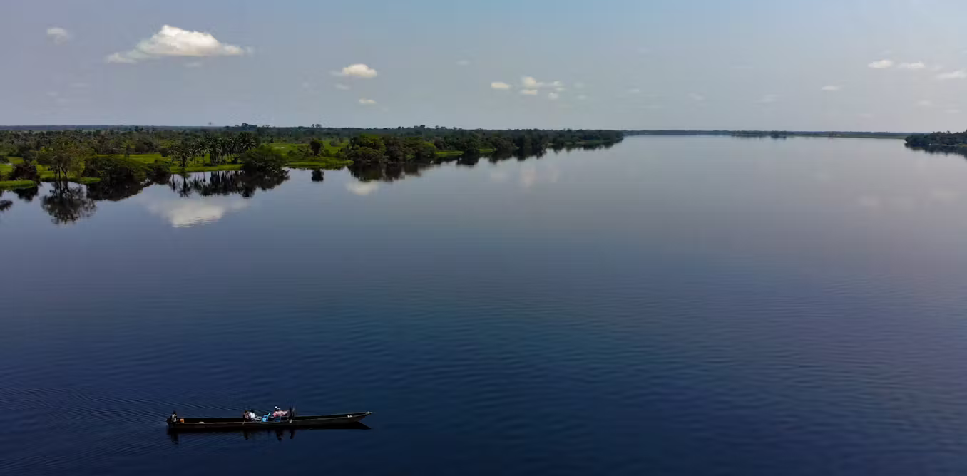 Ruki River blackwater wetlands with flooded forests, traditional fishing canoe, and reflections in Équateur Province, Democratic Republic of Congo